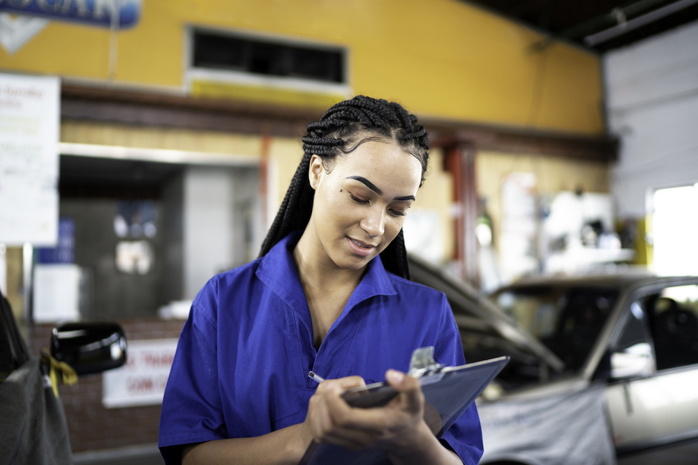 young woman in blue marking notes in front of cars