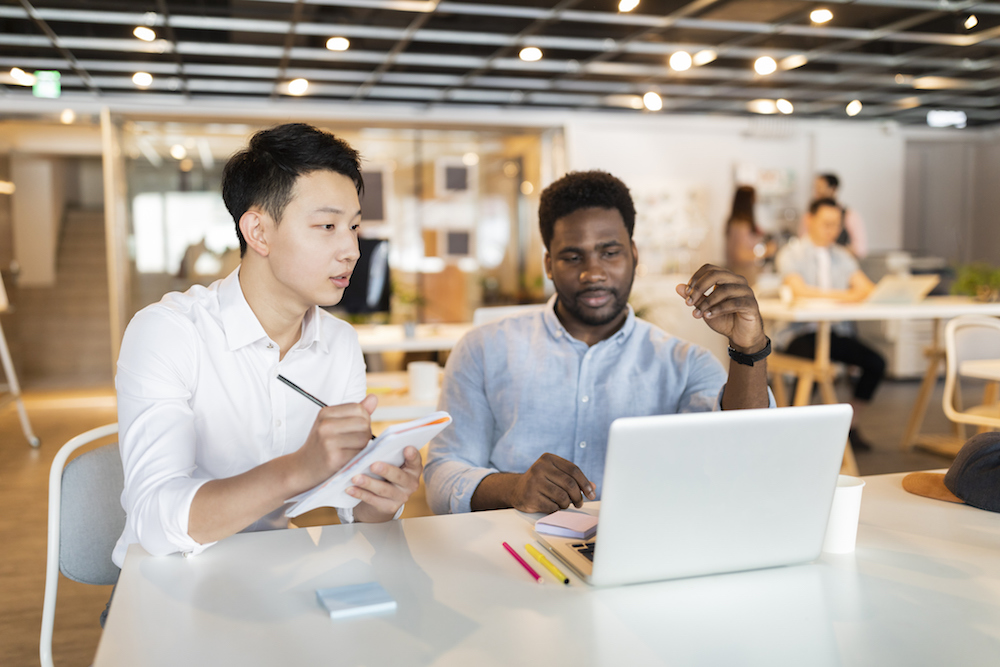 two young men, one pointing to laptop and one taking notes