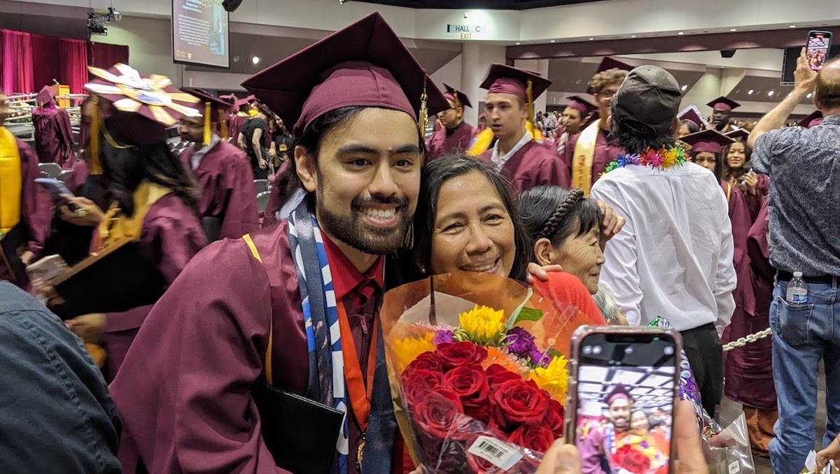 young man with grad cap and gown posing for photo with smiling woman and flowers