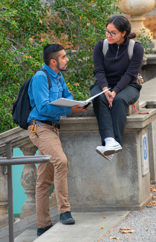 two students outside talking with open binder